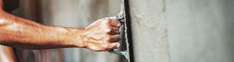 Nahaufnahme der Hand eines Arbeiters, der eine Wand verputzt